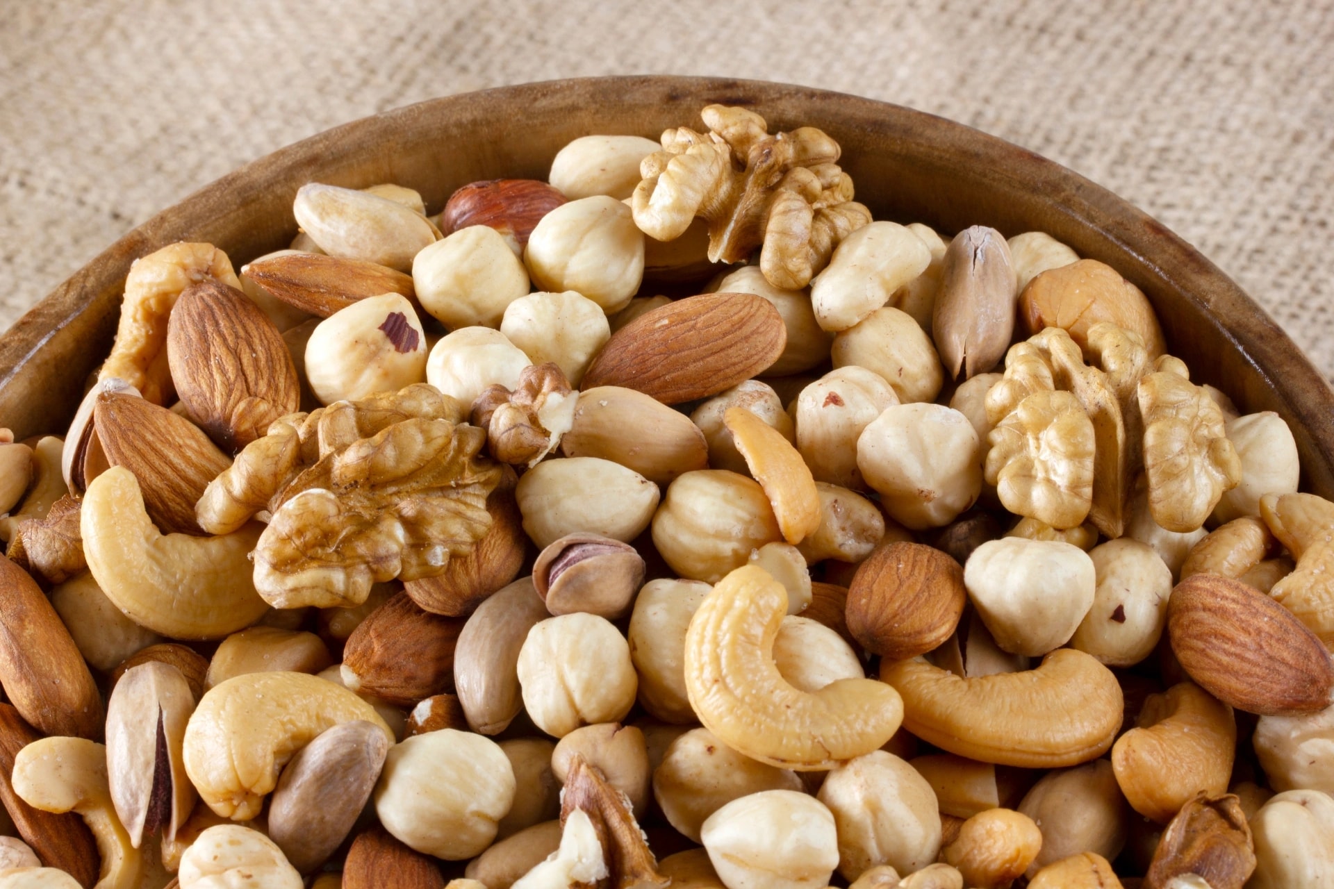 Ciotola di legno colma di frutta secca mista: noci, mandorle, nocciole, anacardi e pistacchi